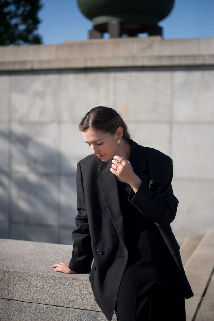 Female model sitting on concrete wall, wearing black blazer.