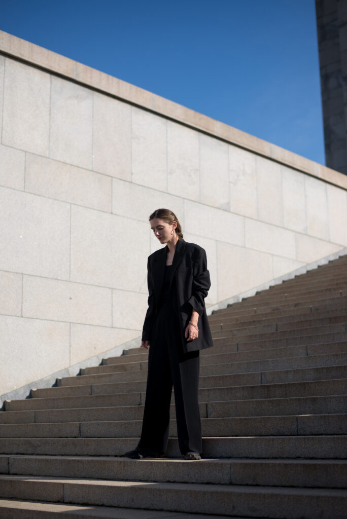 Blonde female model standing on concrete monumental stairs, wearing black minimal clothing.