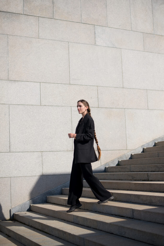 Blonde female model walking on concrete monumental stairs, wearing black minimal clothing.