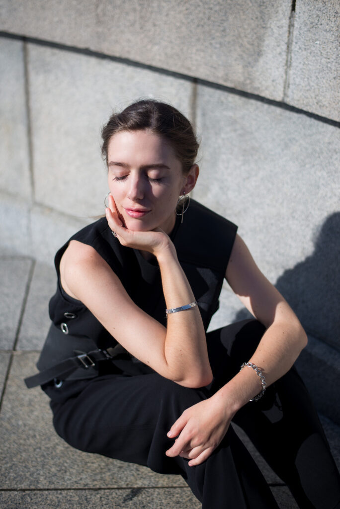 Female model sitting in sunlight against concrete wall, adorned in silver jewellery.